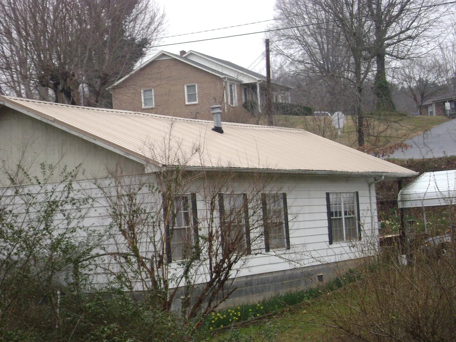 Tan metal roof on a white sided house set into a hillside — Commercial Roofing by Roofing Brothers in Vernon Rockville